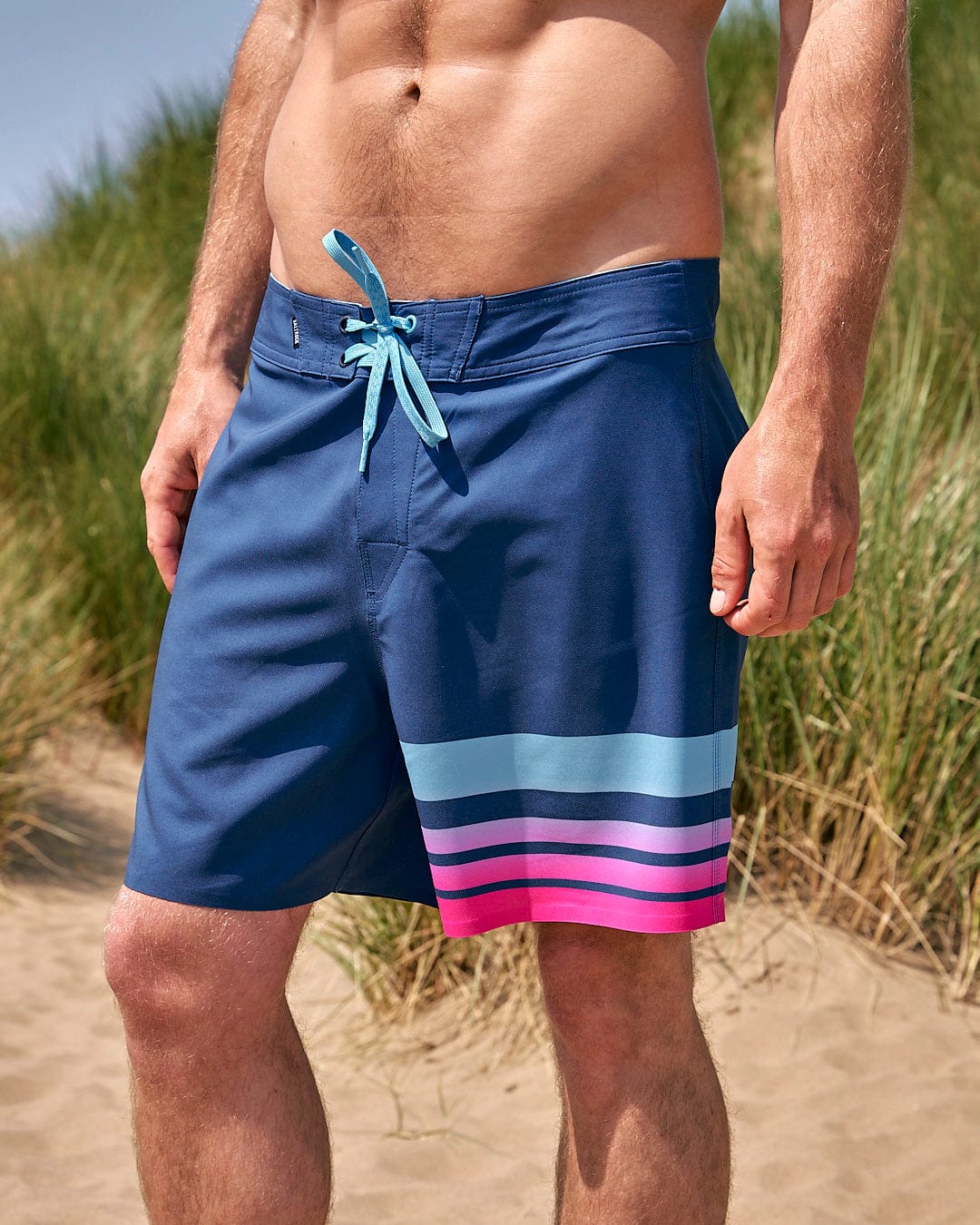 A man is standing in the sand wearing Saltrock's Splash Gradient - Mens Boardshort - Dark Blue.