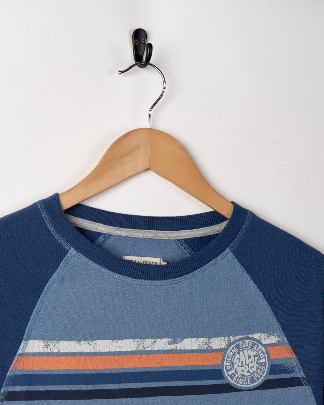 A spray stripe Saltrock blue and gray striped children's sweater with Raglan sleeves hanging on a wooden hanger against a white background.