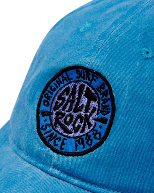 Close-up of a blue SR Original Cap featuring a branded badge for Saltrock with the text "original surf brand since 1988".