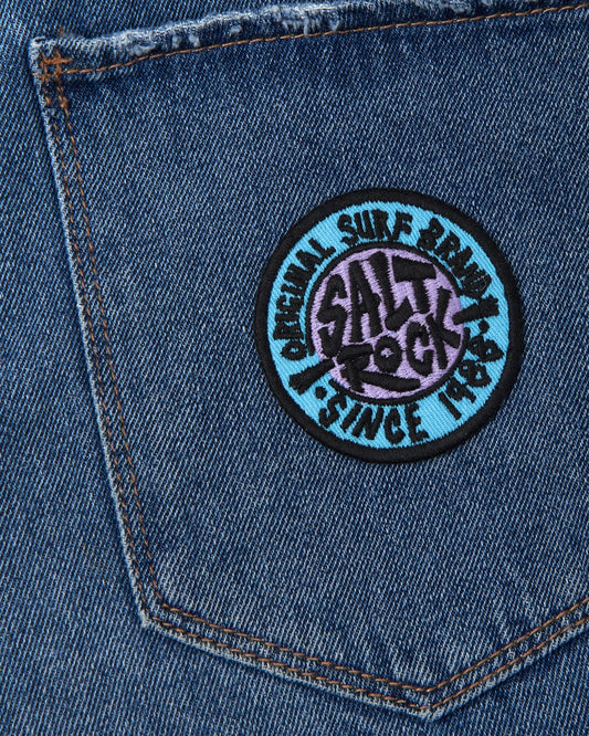 A close-up of a denim fabric with a circular Saltrock branding iron-on patch featuring the SR Original - Patches - Blue design.