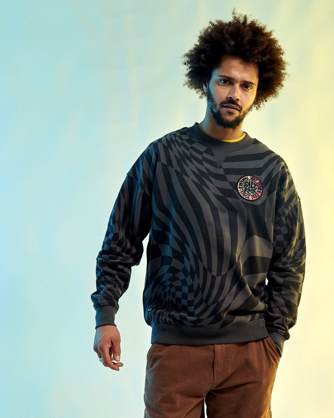 Someone wears the Saltrock SR Warp Men's Oversized Grey Sweat paired with brown pants set against a gradient background.