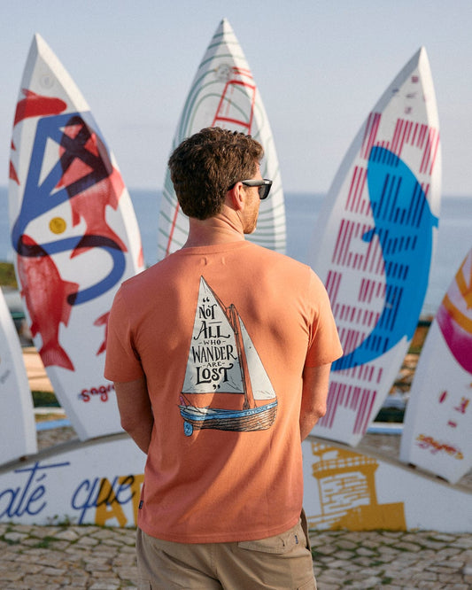 A group of people standing in front of a row of Saltrock Lost Ships Mens Short Sleeve T-Shirt - Orange branding surfboards.