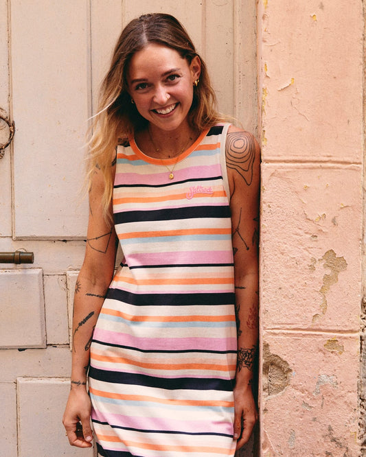 A woman with tattoos smiles in a Saltrock Juno Womens Midi Dress - Multi standing against a textured wall.