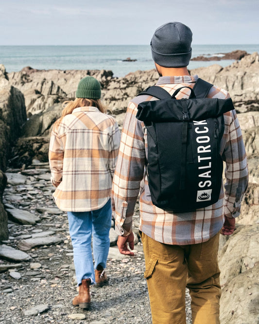 Two people hiking along a durable and water-resistant rocky path, carrying Saltrock Streamline Backpacks in black on their backs.