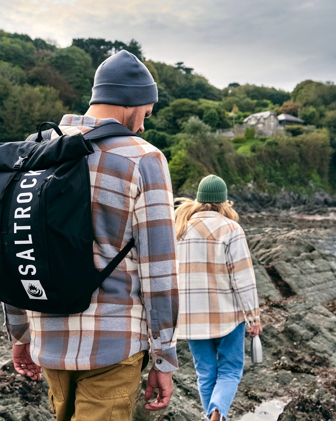 A man and woman walking along a rocky beach with a Saltrock Streamline Backpack in Black.