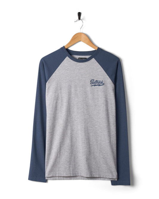 A Saltrock Strike Logo - Mens Long Sleeve Raglan T-Shirt in Grey Marl and navy blue hanging on a wooden hanger against a white wall.