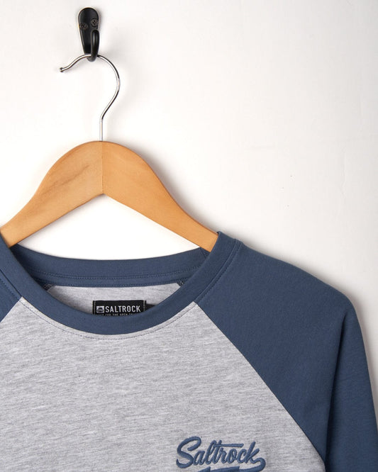 A Saltrock branded Strike Logo - Mens Long Sleeve Raglan T-Shirt in Grey Marl and blue, hanging on a wooden hanger against a white background.