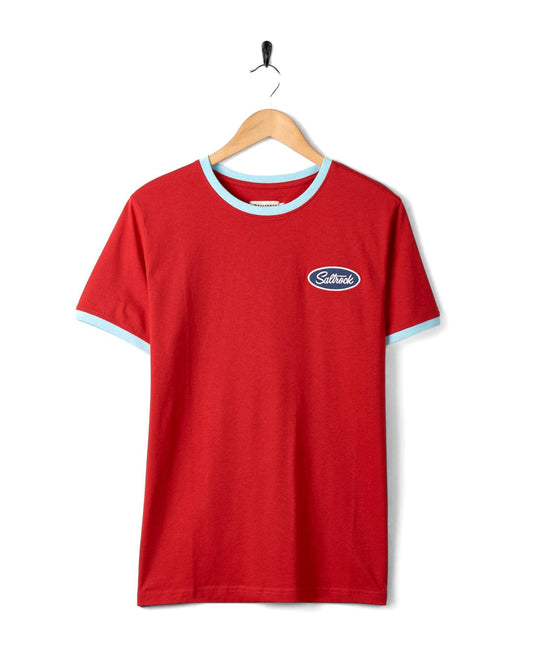 Saltrock's Striker Ringer - Mens Short Sleeve T-Shirt in Red with contrasting blue collar and sleeve edges hanging on a hook against a white background.
