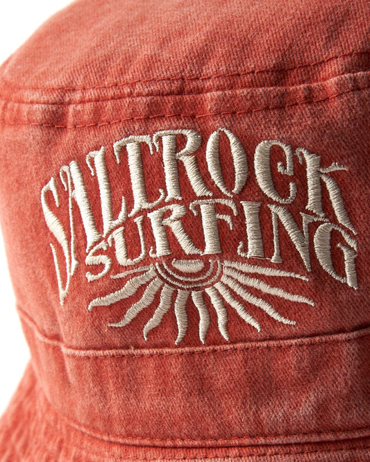 Close-up of embroidery on a red cotton Sunburst Bucket Hat - Burnt Orange with the words "Saltrock surfing" in silver thread.