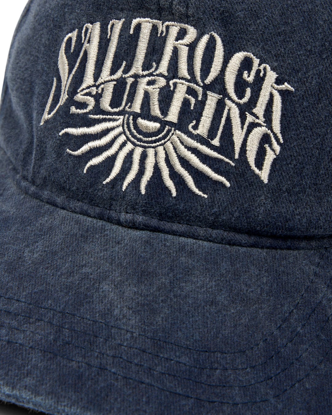 Close-up of a navy blue cotton Sunburst Cap - Dark Blue with Saltrock branding embroidered on it in white thread.