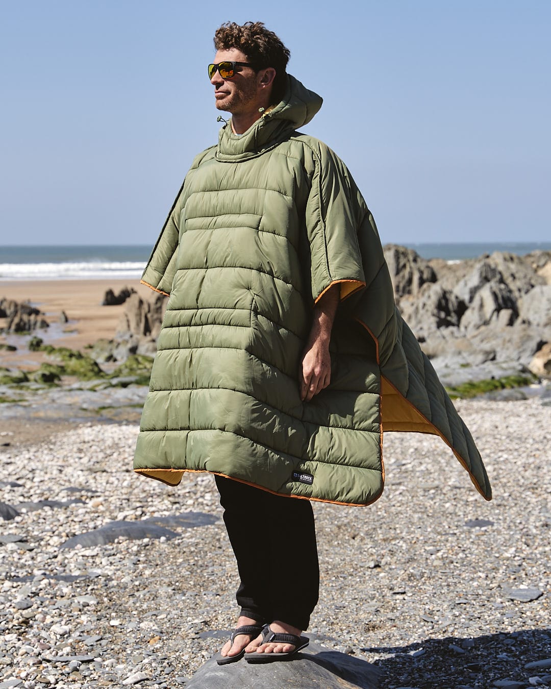 A man in a Sunset - Packable Reversible Poncho - Yellow by Saltrock, standing on a rock.