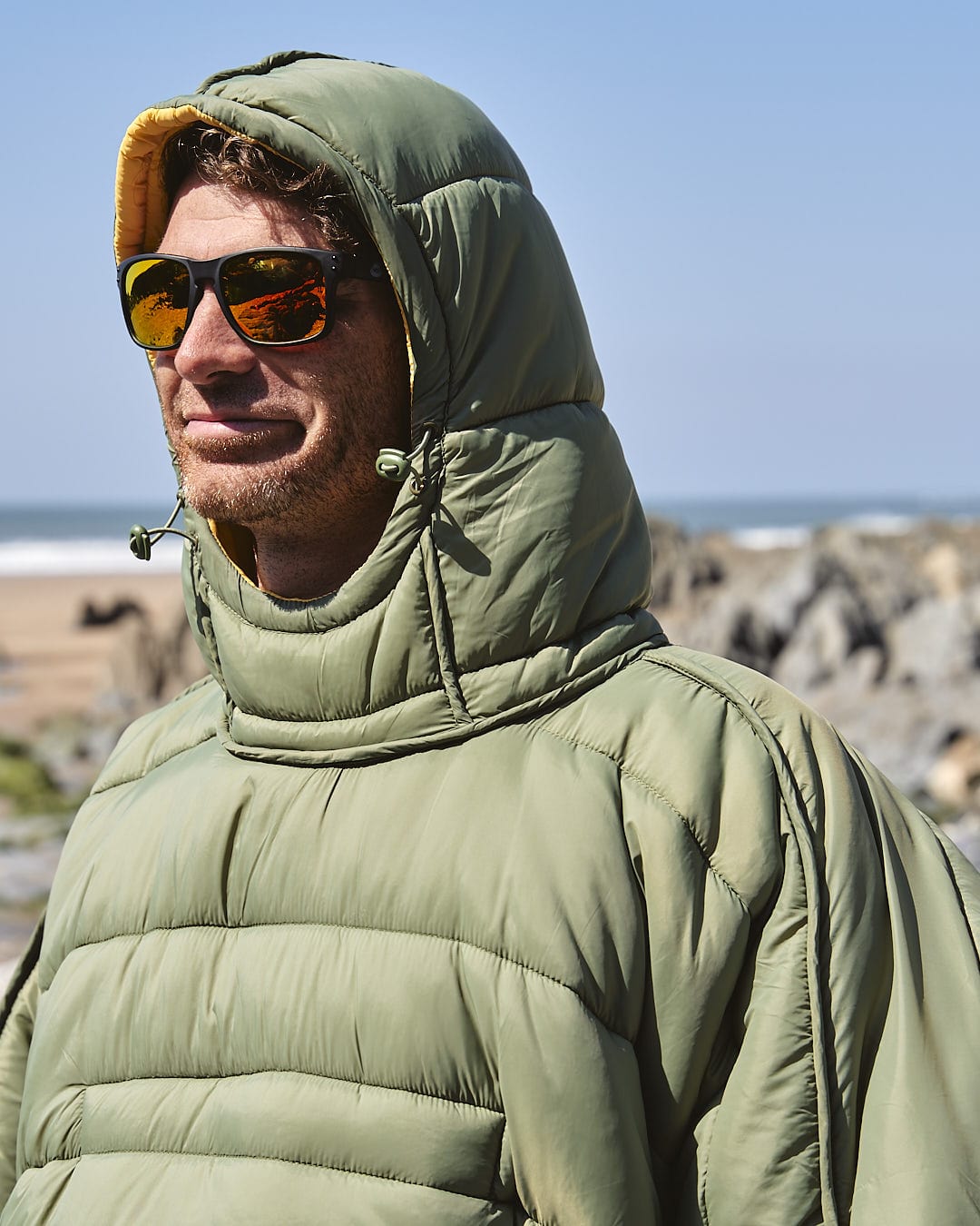 A man in a Saltrock green puffy jacket standing on the beach.