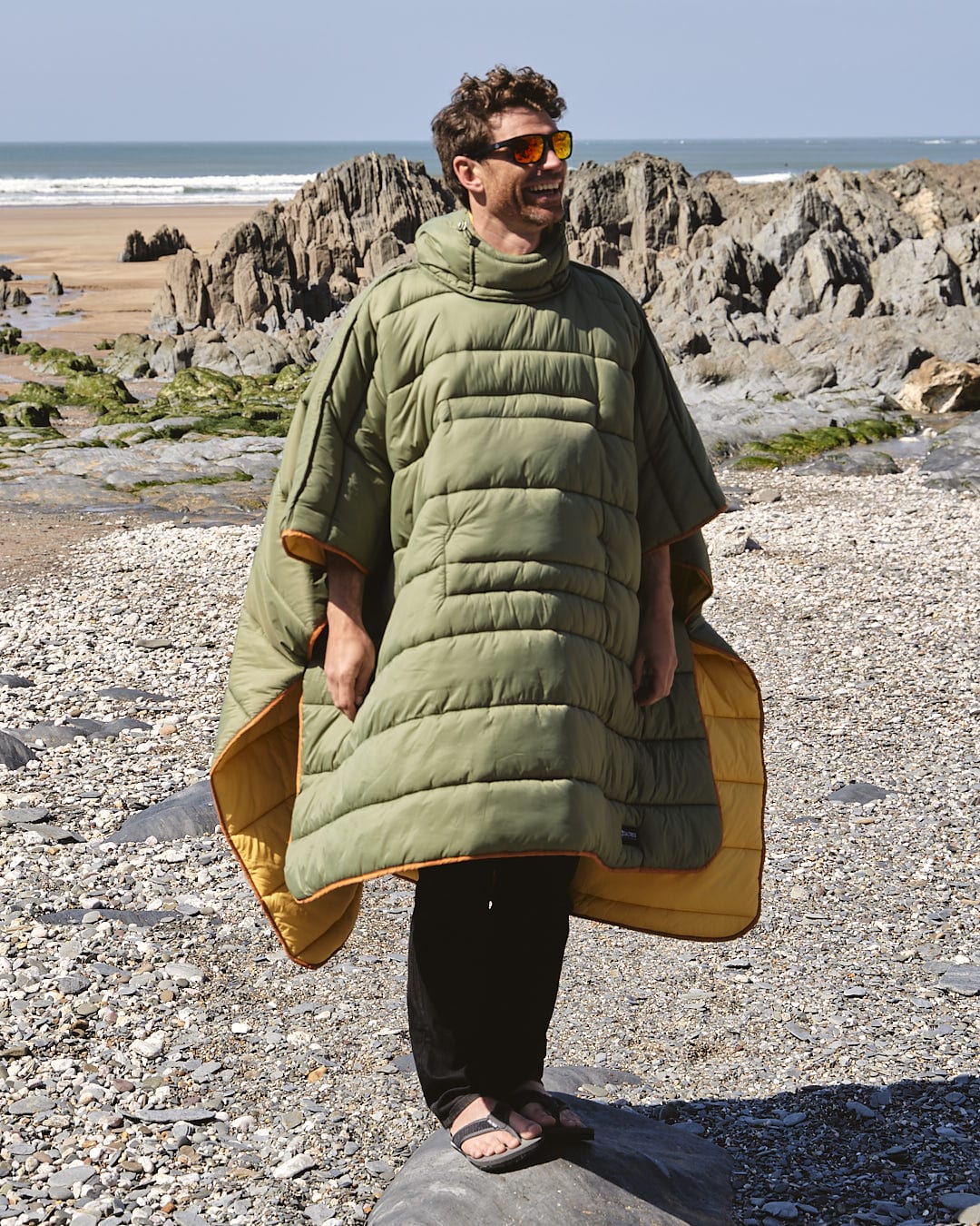 A man in a yellow Sunset - Packable Reversible Poncho by Saltrock standing on a rock.