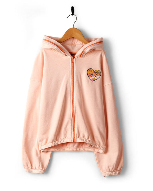 A Sunshine State - Kids Zip Hoodie in Peach by Saltrock, with a front zipper and a small heart emblem on the left chest, hanging on a wooden hanger against a white background.