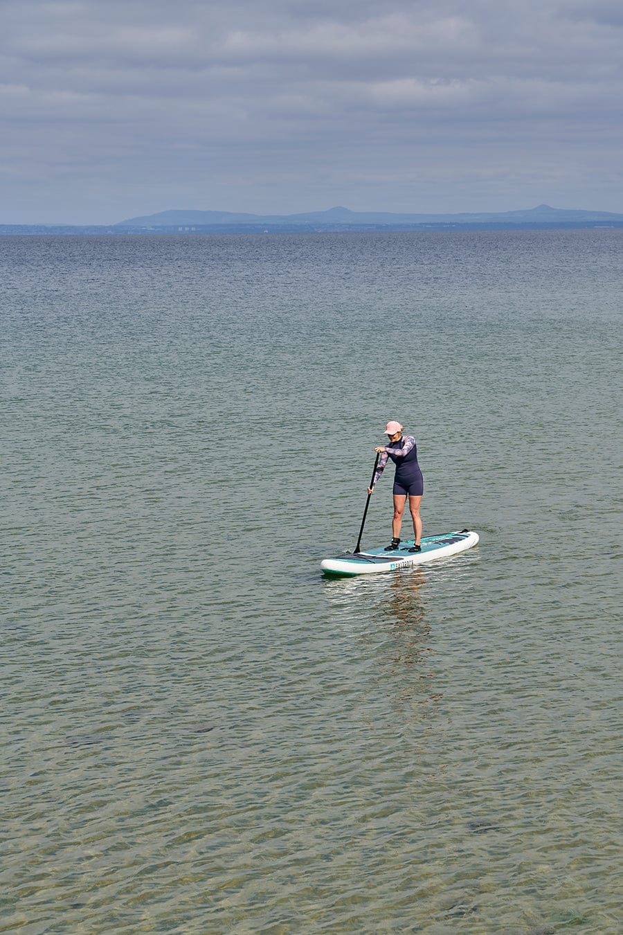 A man standing on a Shockwave - Inflatable Stand Up Paddle Board - Turquoise by Saltrock in the water.