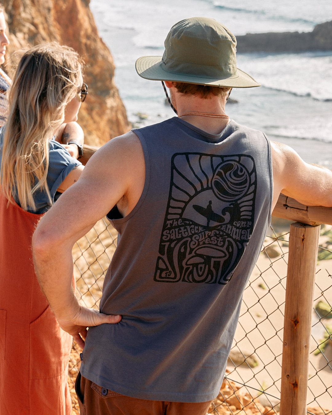 A group of people standing on a fence looking at the ocean, some wearing Saltrock's Surf Fest Mens Vest in Dark Grey.
