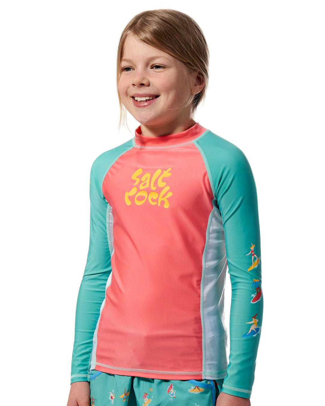 A girl wearing a Surf Sister - Kids Long Sleeve Rashvest - Coral/Turquoise by Saltrock.