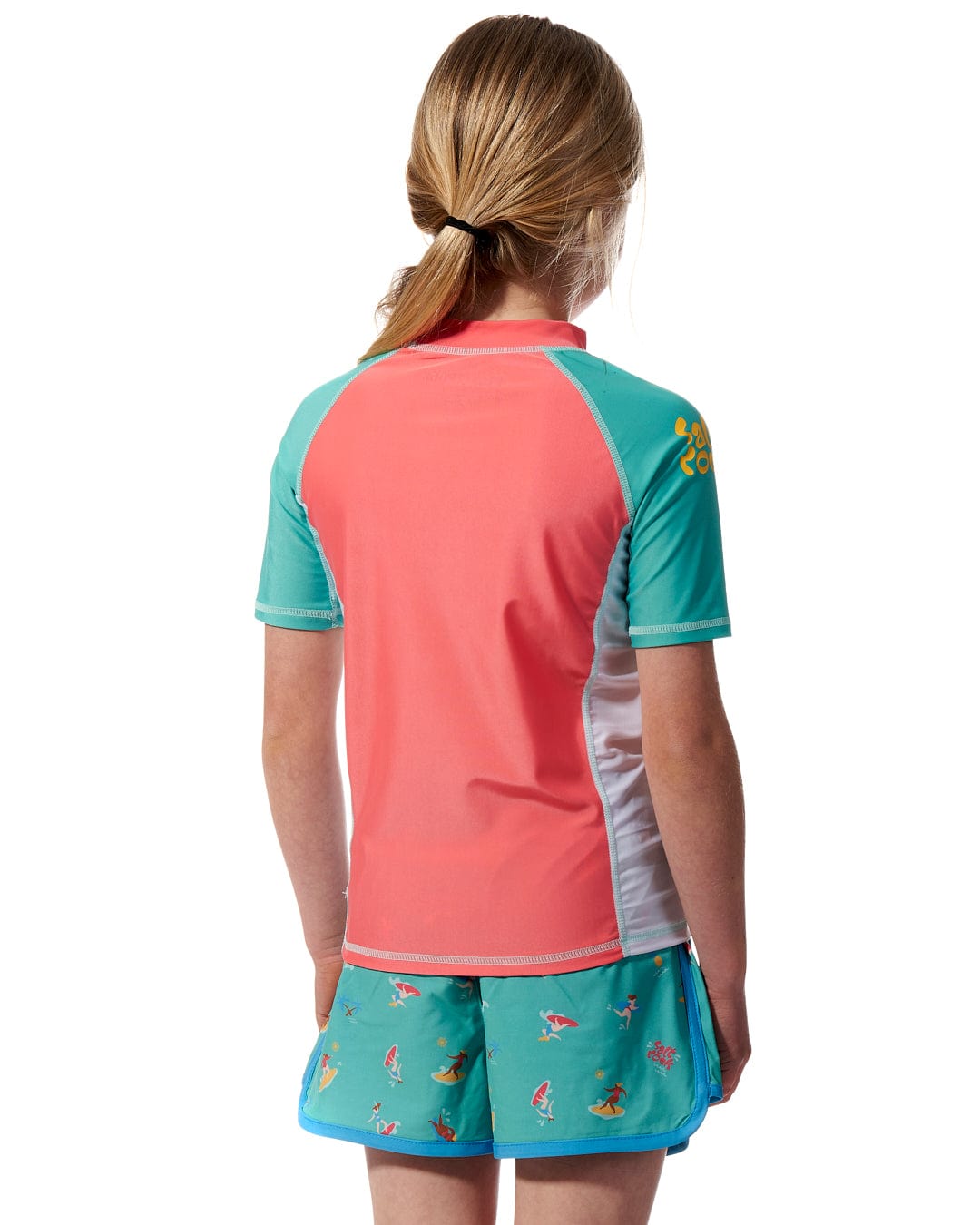 The back view of a girl wearing a Surf Sister - Kids Short Sleeve Rashvest in Coral/Turquoise, made by Saltrock.