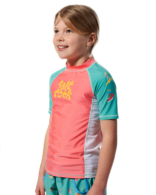 A young girl wearing a Saltrock Surf Sister - Kids Short Sleeve Rashvest in Coral/Turquoise.