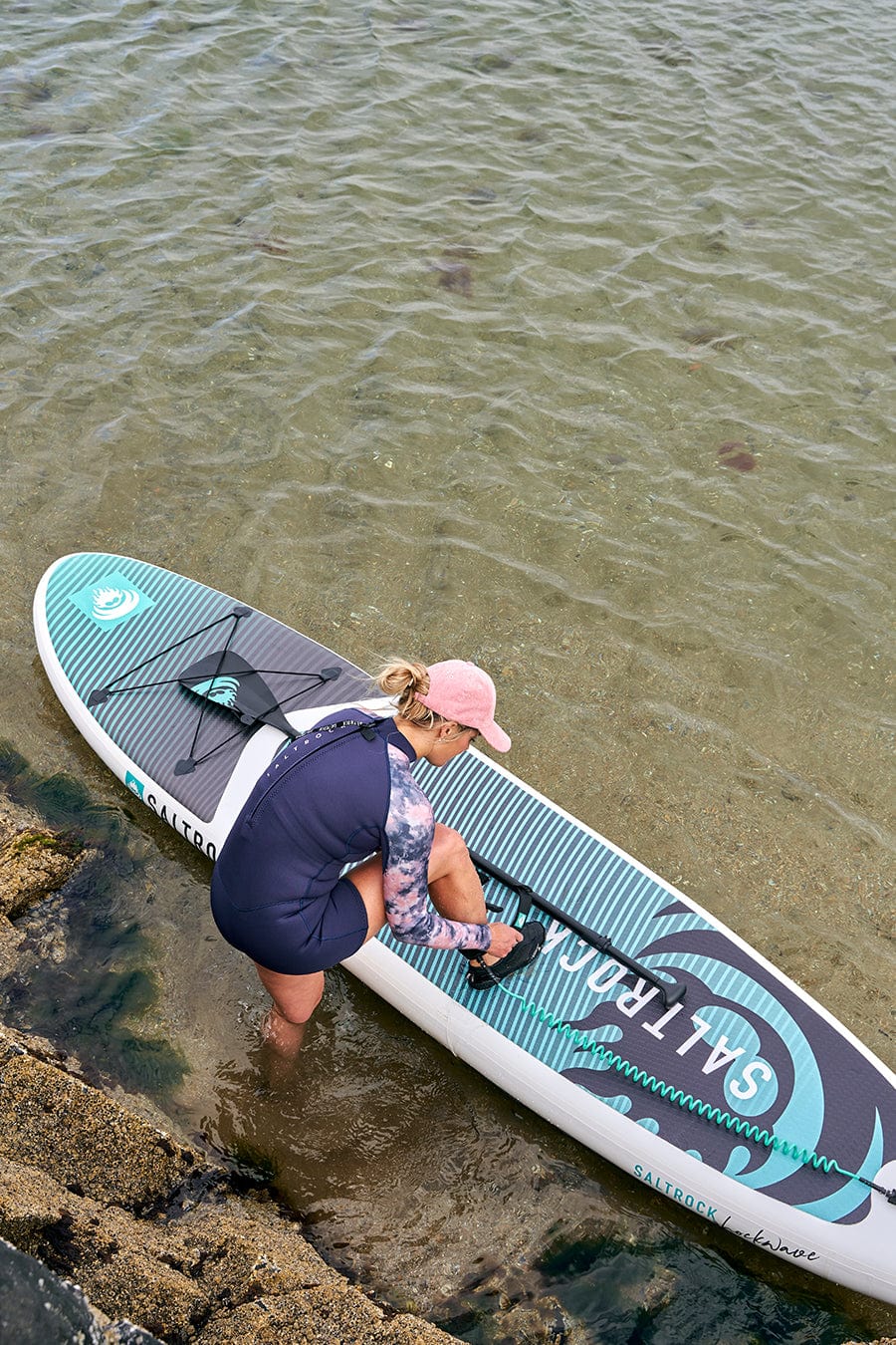 A woman standing on a Saltrock Shockwave - Inflatable Stand Up Paddle Board - Turquoise in the water.