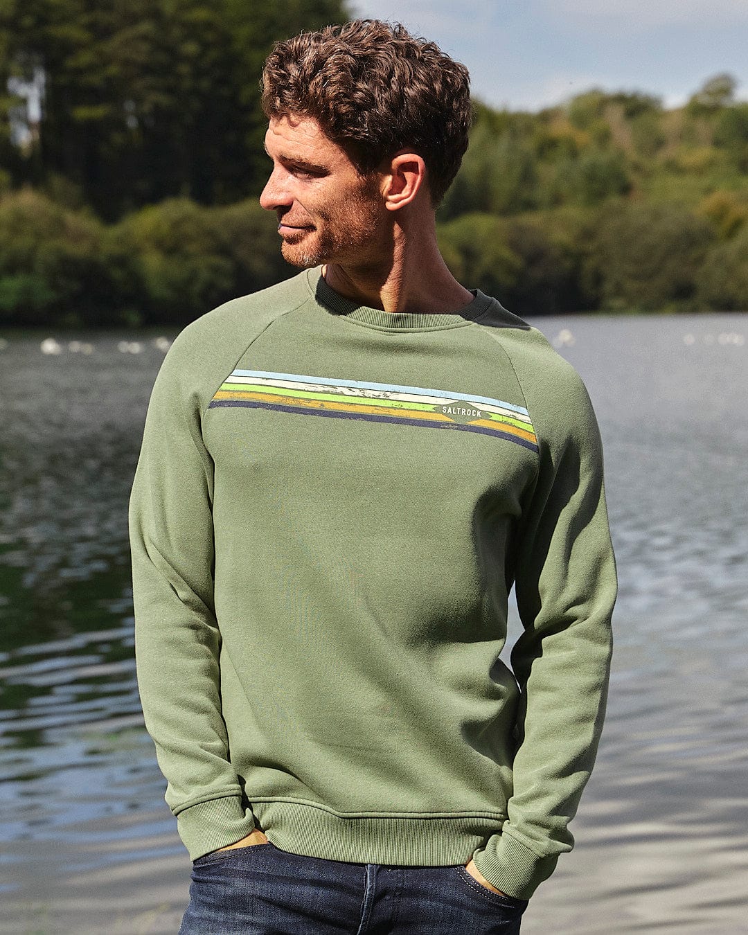 A man walking on a beach with a Saltrock Taped Stripe - Mens Crew Sweat - Green.