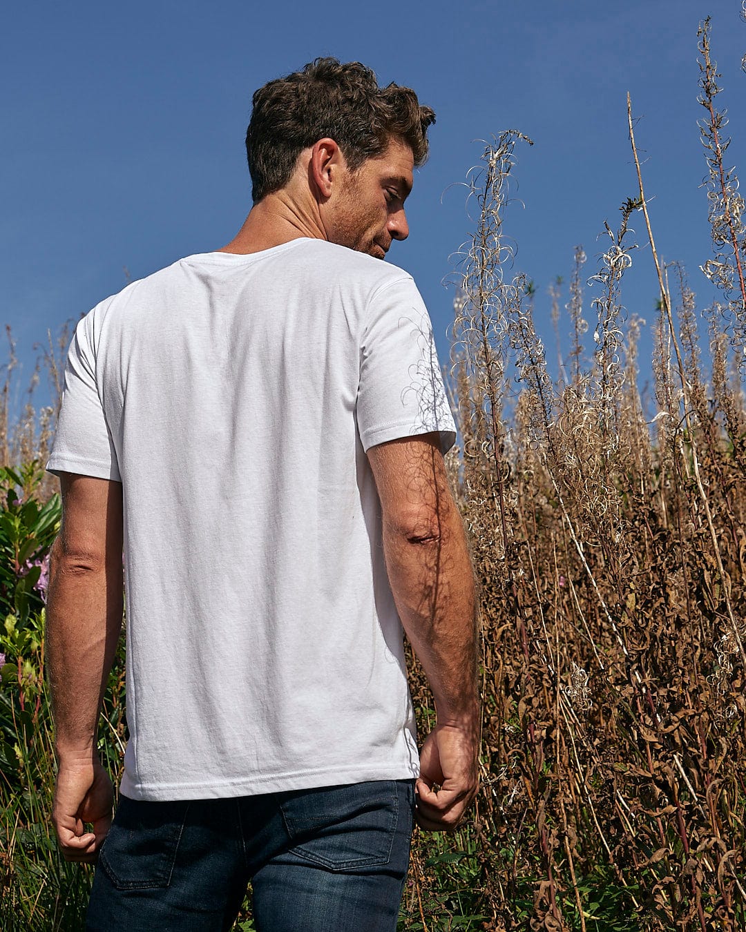 A man wearing a Saltrock Tent Truck - Mens Short Sleeve T-Shirt - White standing outdoors in a field.