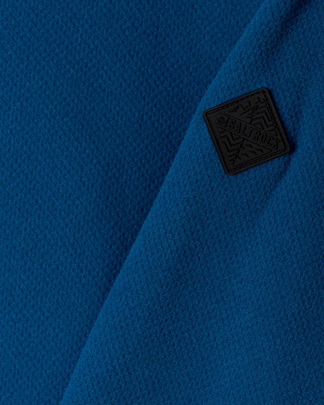 A close up of a Saltrock Theo - Mens 1/4 Neck Fleece - Blue made of polyester fabric with a black patch on it.