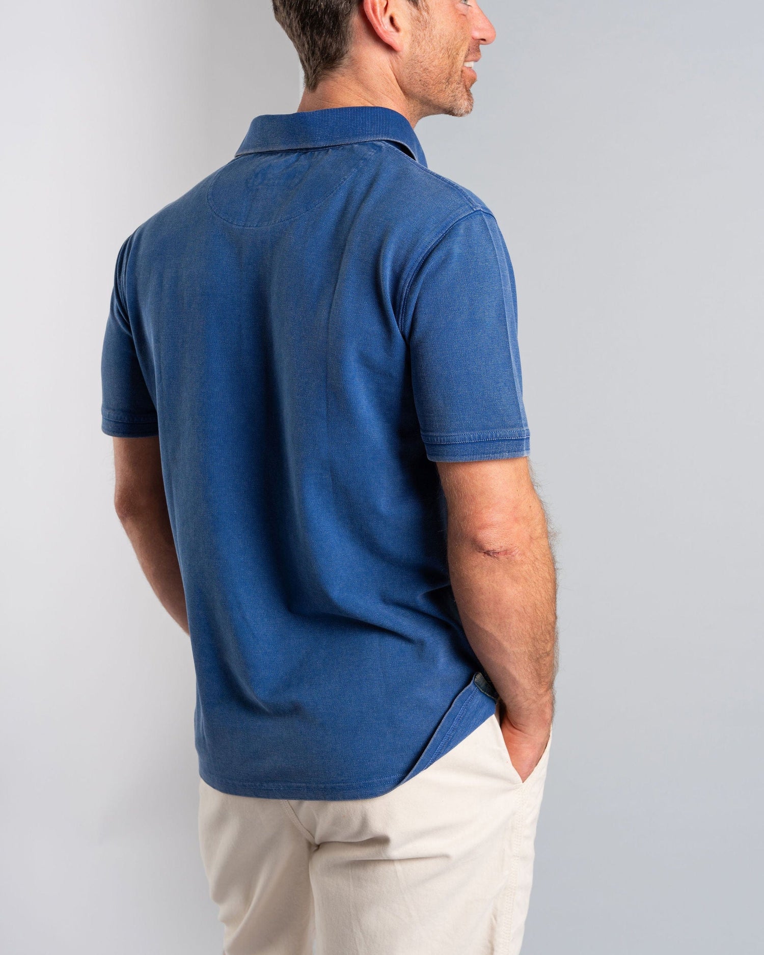 A man stands in side profile, hands in pockets and wearing light pants, showcasing the Saltrock "Seb - Men's Short Sleeve Polo - Blue," made from 100% cotton. Neutral background.