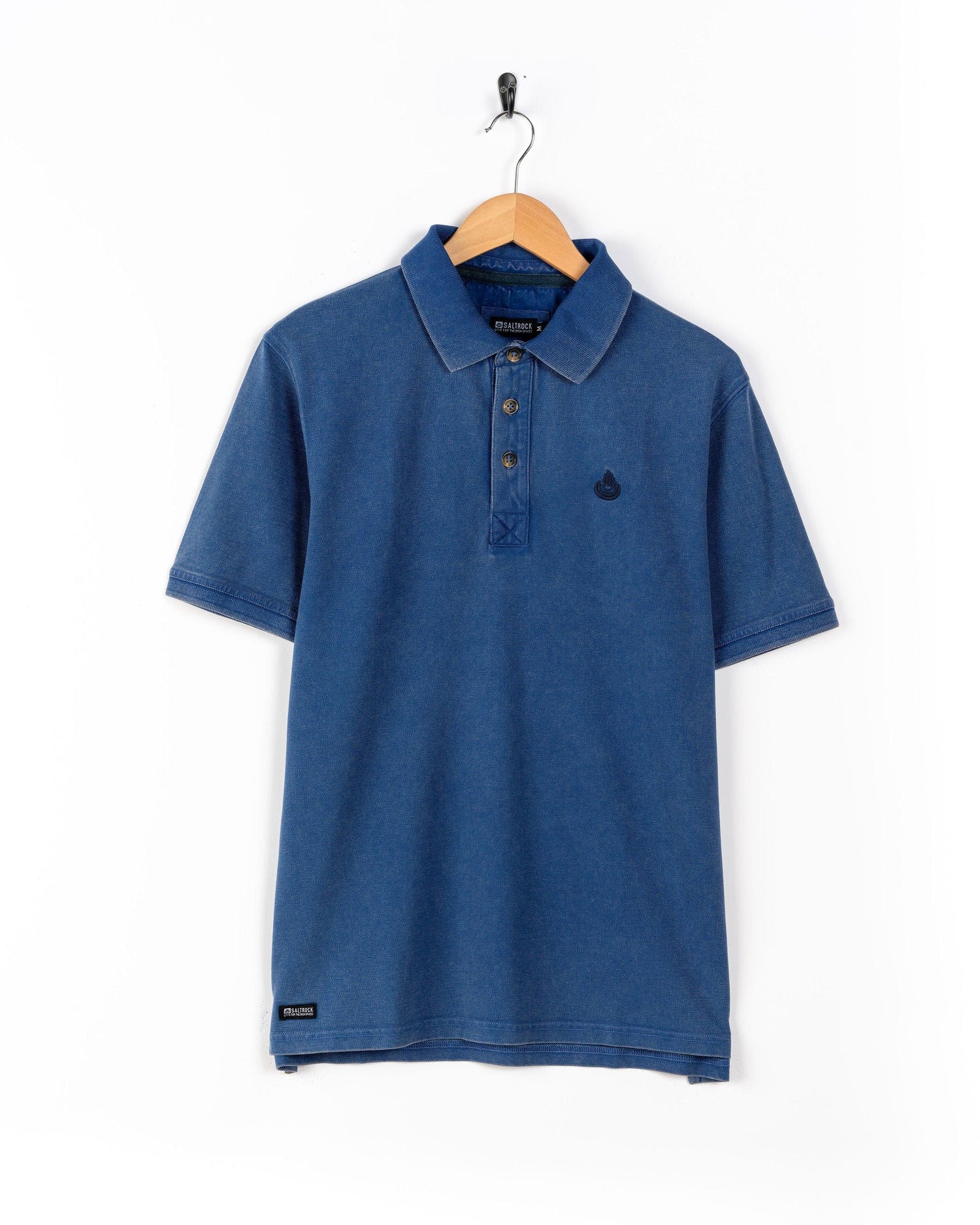 The Seb Men's Short Sleeve Polo by Saltrock is 100% cotton, featuring a three-button placket and the iconic logo on the left chest, shown in blue on a wooden hanger against a white background.