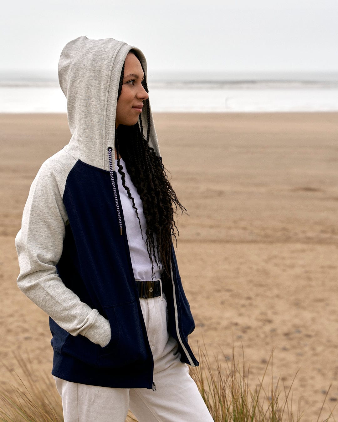 A woman wearing a Saltrock Trademark - Zip Hoodie - Dark Blue hoodie standing on the beach.
