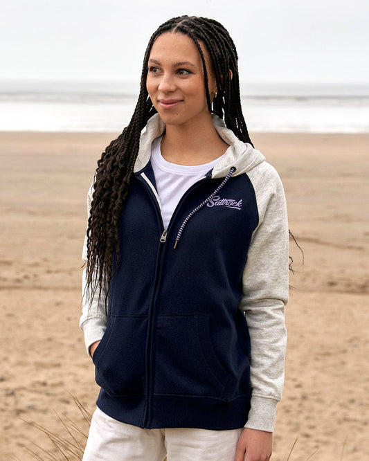 A woman wearing a Saltrock Trademark - Zip Hoodie - Dark Blue standing on a beach.