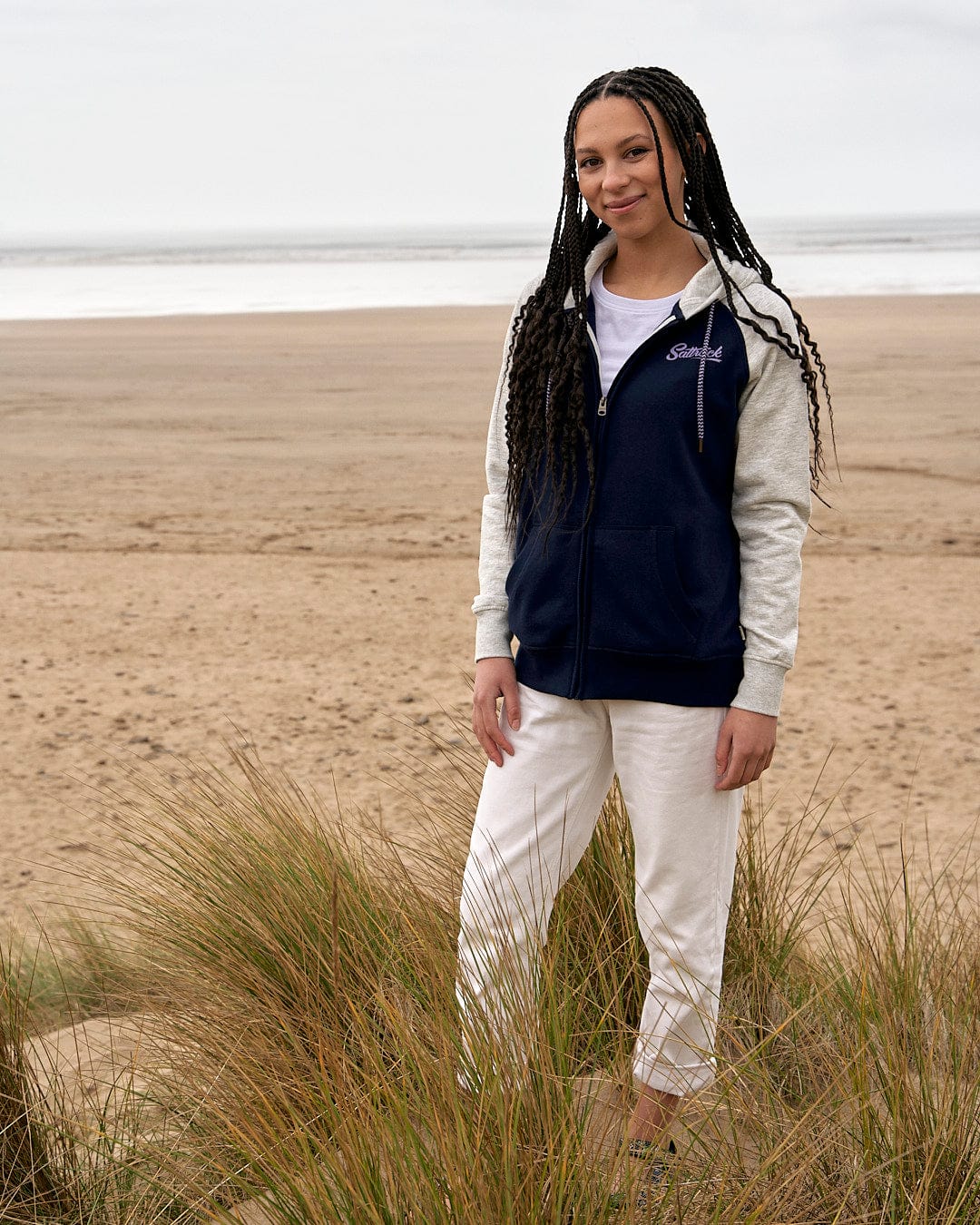 A woman standing on a beach wearing a Saltrock Trademark - Zip Hoodie - Dark Blue.