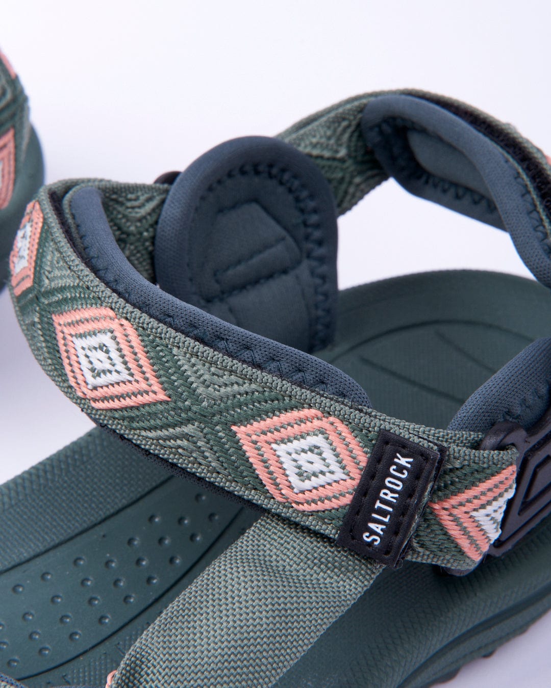 Close-up of a Saltrock green and black Trail Women's Sandal with geometric straps and a label displaying the brand "Saltrock.