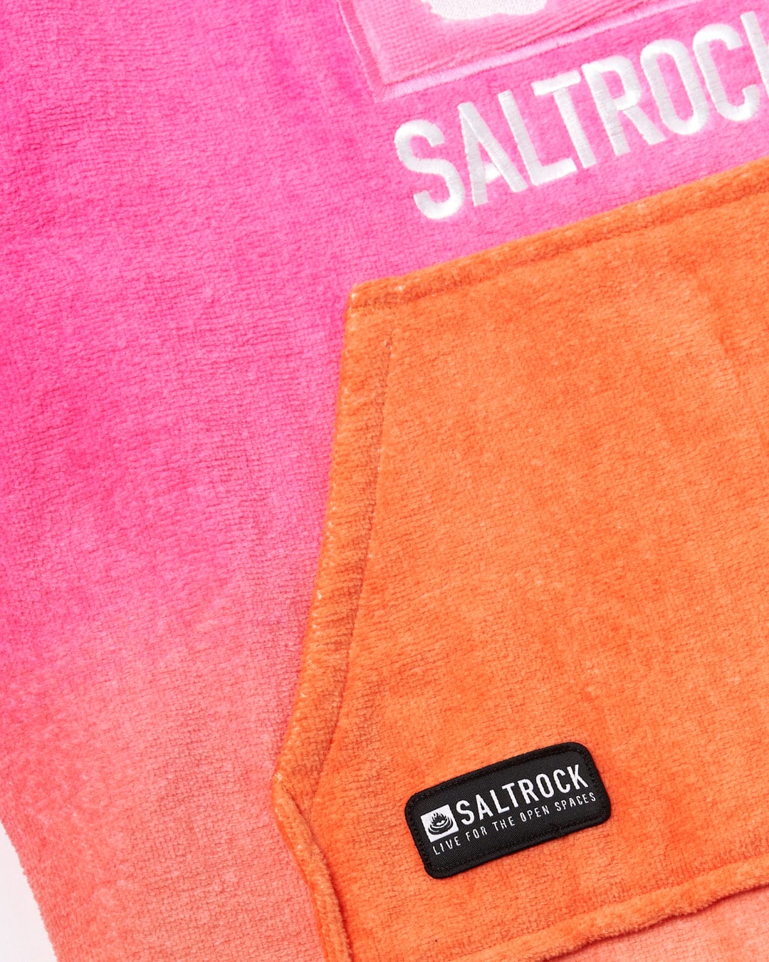 Close-up of a Tropic Dip - Kids Changing Towel - Pink/Orange partially overlaid with an orange pocket featuring a black Saltrock logo patch.