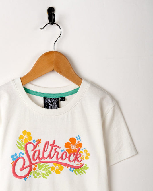 White Tropic - Recycled Kids Short Sleeve T-Shirt with colorful Saltrock print logo, hanging on a wooden hanger against a white wall.