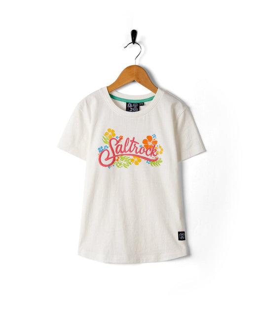 A white graphic t-shirt featuring the word "Tropic" by Saltrock surrounded by colorful floral designs, hanging on a wooden hanger against a white background.