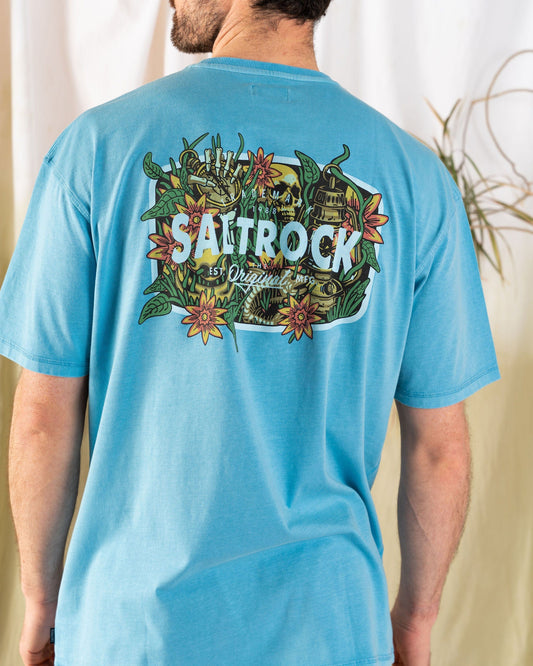 Someone is wearing the Saltrock Jungle Wanderer men's oversized T-shirt in blue, featuring a vibrant floral and nature-themed graphic on the back, made from 100% cotton.