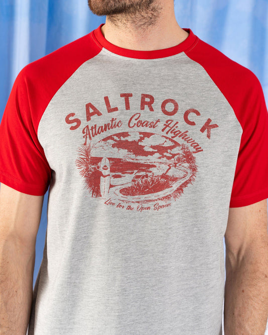 A man wearing the Saltrock AC Highway Men's T-Shirt in grey/red, featuring "Atlantic Coast Highway" and a scenic front print, with a classic crew neck and Saltrock branding.