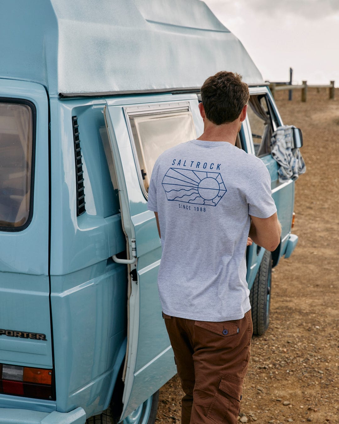 A man standing next to a blue vw camper van, wearing a Vantage Outline - Mens Short Sleeve T-Shirt in Grey Marl with Saltrock branding.