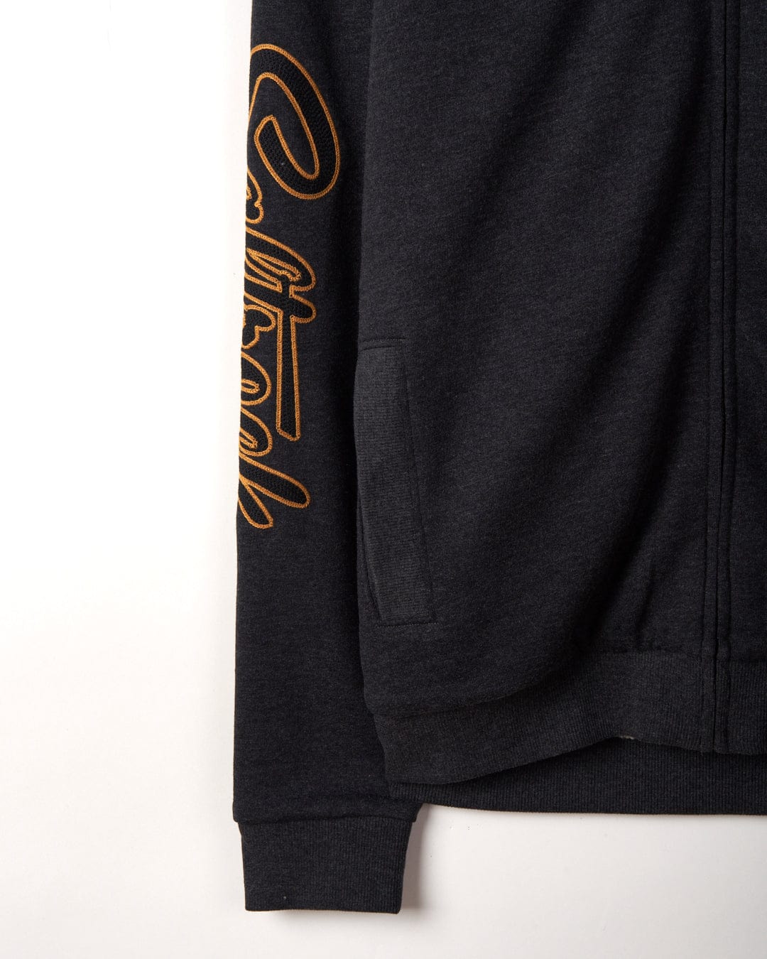 Close-up of a grey Saltrock Vegas Script Mens Borg Lined Zip Hoodie with an embroidered chain stitch orange cursive logo on the sleeve, displayed against a white background.