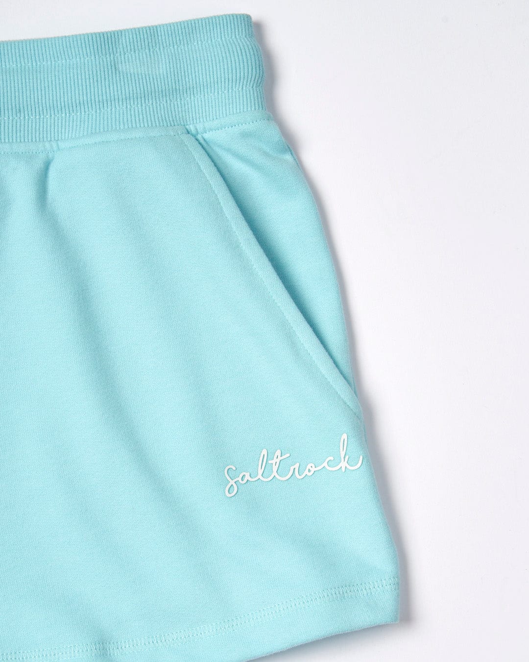 Close-up of a light blue Velator - Womens Short material, part of a garment with a ribbed waistband and the word "Saltrock" embroidered in white.