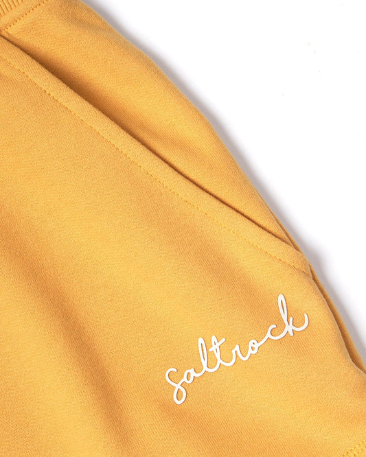 Close-up of a mustard yellow Velator - Womens Short with the word "Saltrock" embroidered in white script on it.