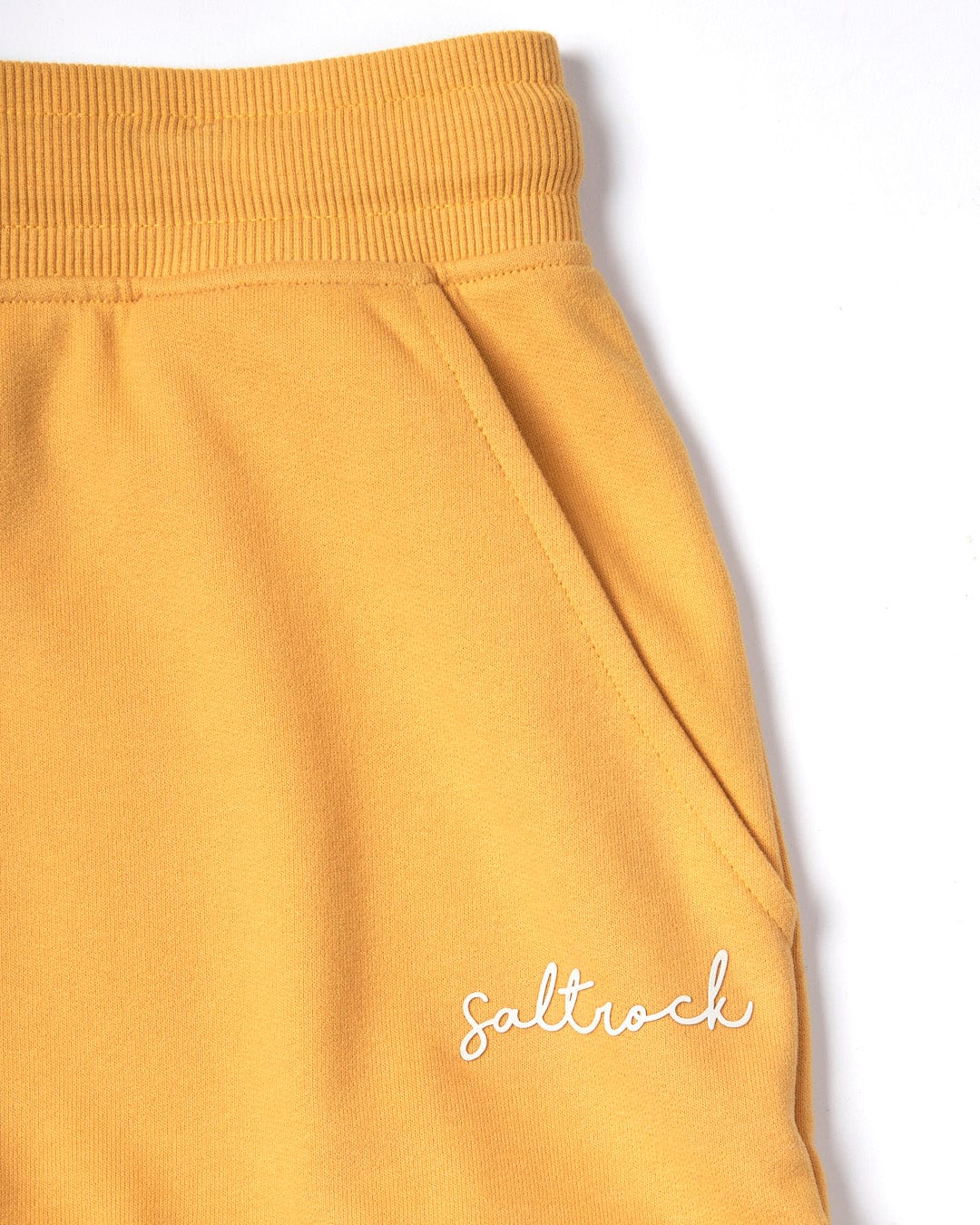 Close-up of Saltrock Velator - Womens Short - Yellow sweatpants with an elasticated waist and "Saltrock" embroidered near the pocket on a white background.
