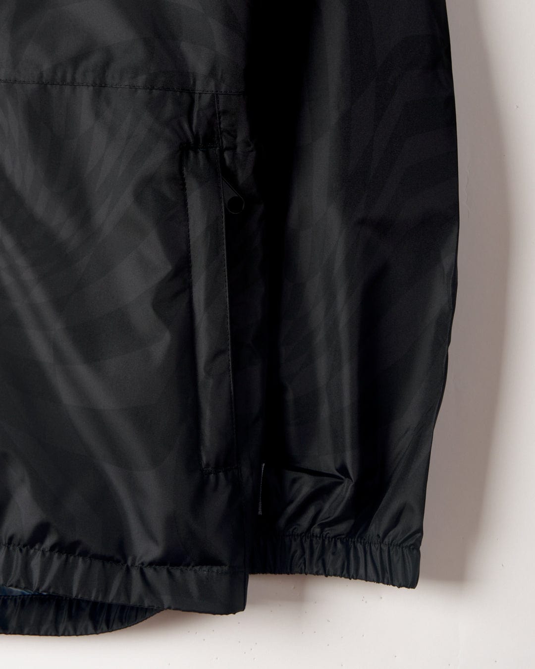 Close-up of a Warped - Kids Waterproof Packable Jacket in Black by Saltrock showing detail of the fabric and side pocket with an elastic hem.