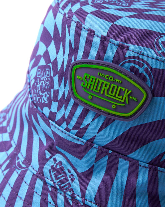 Close-up of a colorful patterned fabric with a bright green Saltrock rubber badge, featuring the Saltrock Warp Icon - Kids Bucket Hat - Blue.