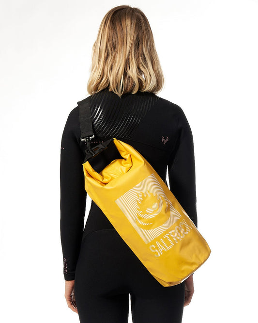A woman wearing a Saltrock yellow wetsuit and a Wave - 10L Drybag - Yellow waterproof dry bag.