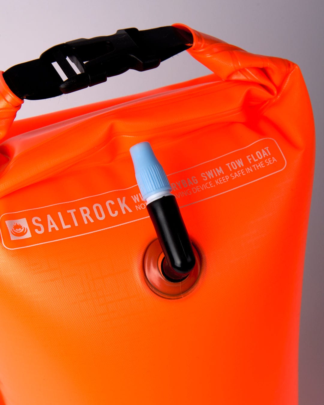A close-up of a bright orange, waterproof Saltrock Wild Drybag/Inflatable Swim Tow Float with an inflation valve and clip visible, perfect for cold water swimming.