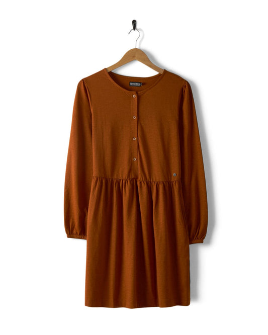 The Winnie women's dress in dark orange from Saltrock, crafted from Jersey slub fabric, features long sleeves, buttons down the front, and an elasticated waist, elegantly displayed on a wooden hanger against a crisp white background.
