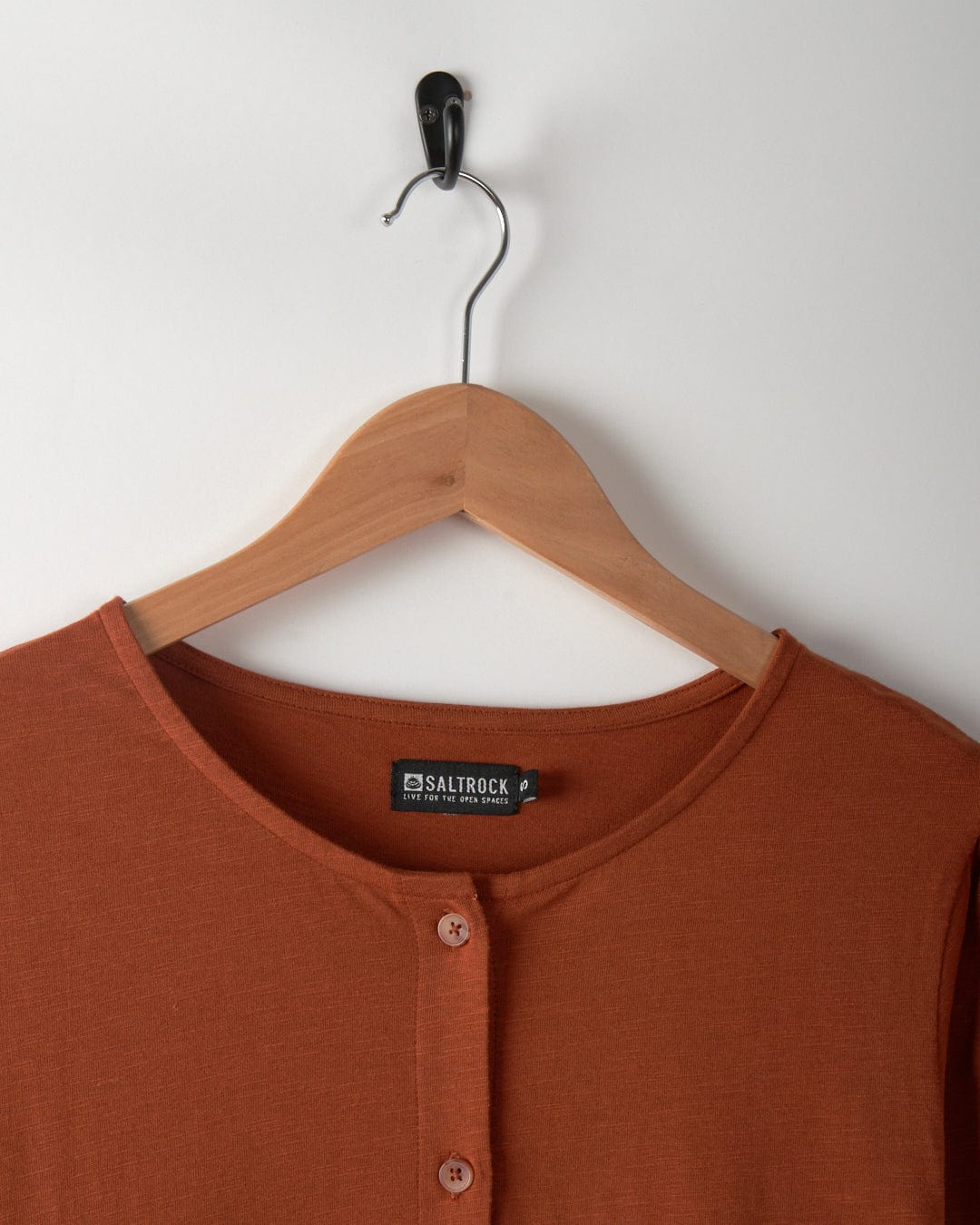 The dark orange Winnie dress from Saltrock, crafted from Jersey slub fabric, elegantly hangs on a wooden hanger against a white wall.