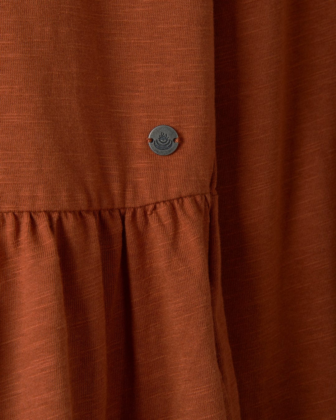 Close-up of the Winnie women's dress in dark orange by Saltrock, featuring a jersey slub fabric with a single button.